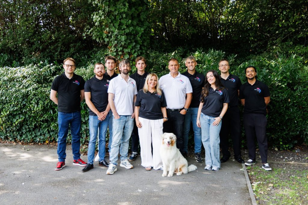 group photo of people and a dog stood together in front of a bush